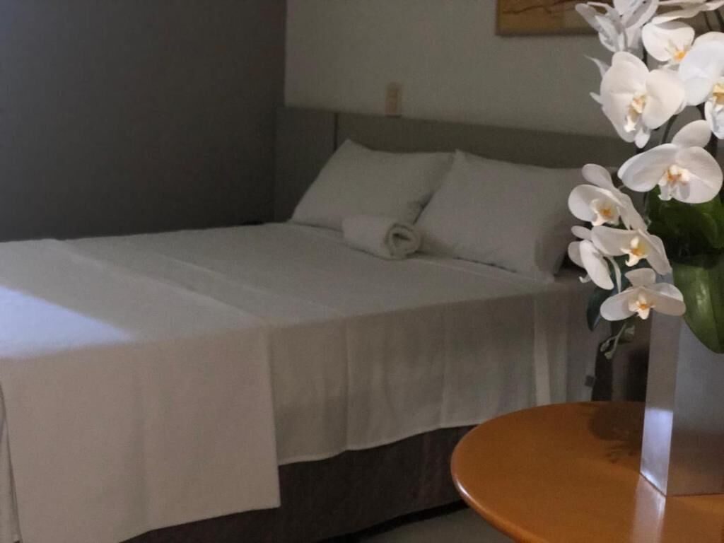 A neatly made bed with a white bedspread, a wooden nightstand, and a vase with white flowers.