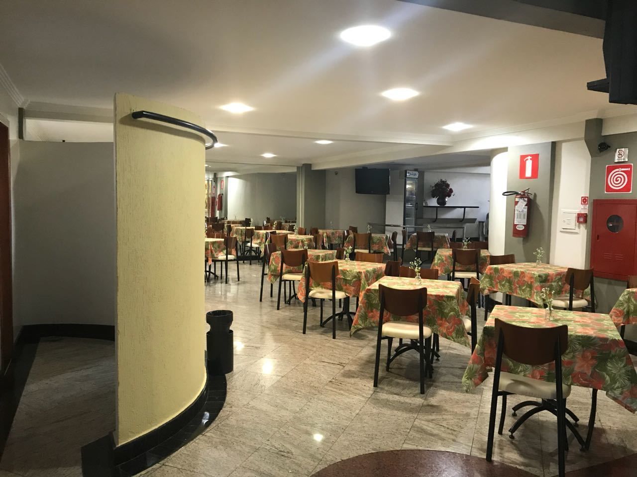 Un comedor espacioso con varias mesas y sillas, un extintor y un televisor montado en la pared.