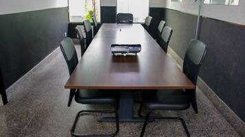 Uma sala de conferências com uma mesa comprida, cadeiras pretas e um projetor.