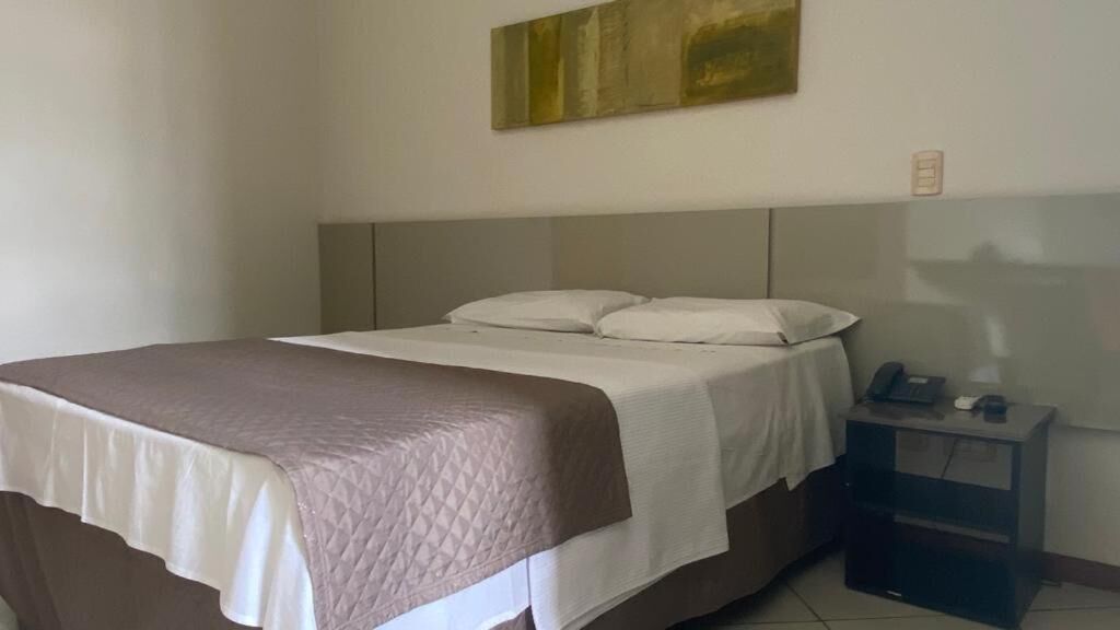 A hotel room with a bed, bedside table, and a painting on the wall.