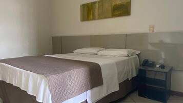 A hotel room with a bed, bedside table, and a painting on the wall.