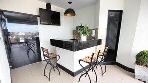 Une cuisine moderne avec un plan de travail noir, deux tabourets de bar, une plante en pot et un téléviseur fixé au mur.