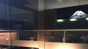 Un intérieur moderne avec une cloison en verre, un sol carrelé et une vue sur le paysage urbain illuminé la nuit.