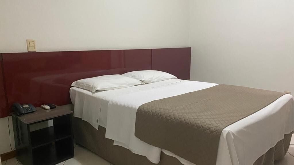 Una cama individual con cabecera, una mesita de noche con un teléfono y un enchufe de pared.