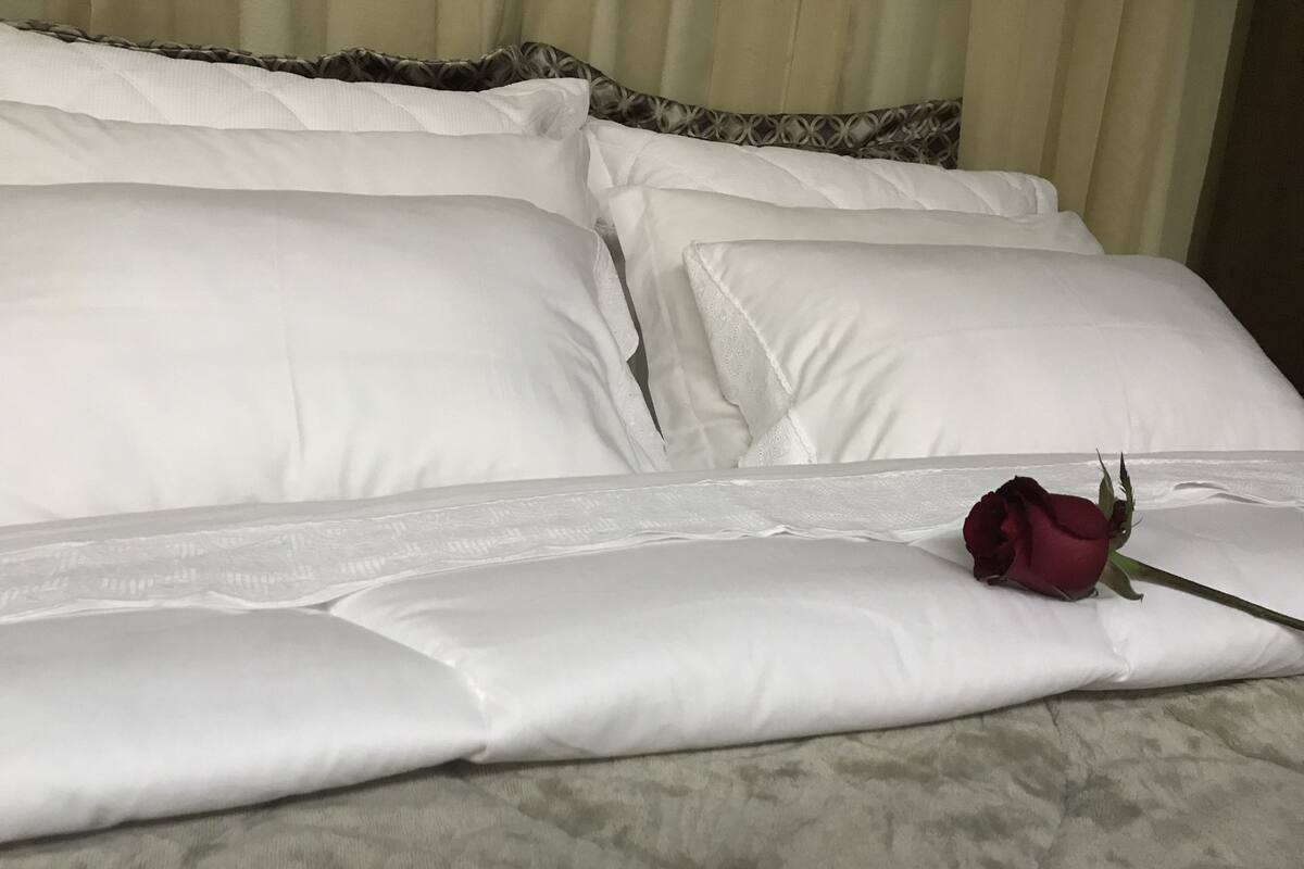 Una cama bien hecha con sábanas blancas y una única rosa roja.