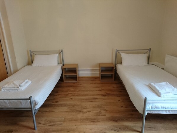 A room with two single beds, each with a wooden nightstand and a white pillow.