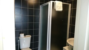 Casa de banho com paredes revestidas a preto, sanita branca e cabine de duche com vidro.