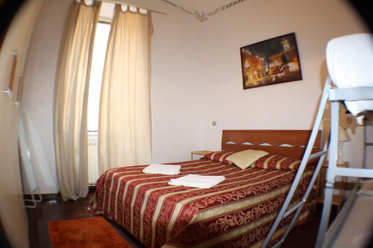 A bedroom with a bed, a window with curtains, a painting on the wall, and a white chair.