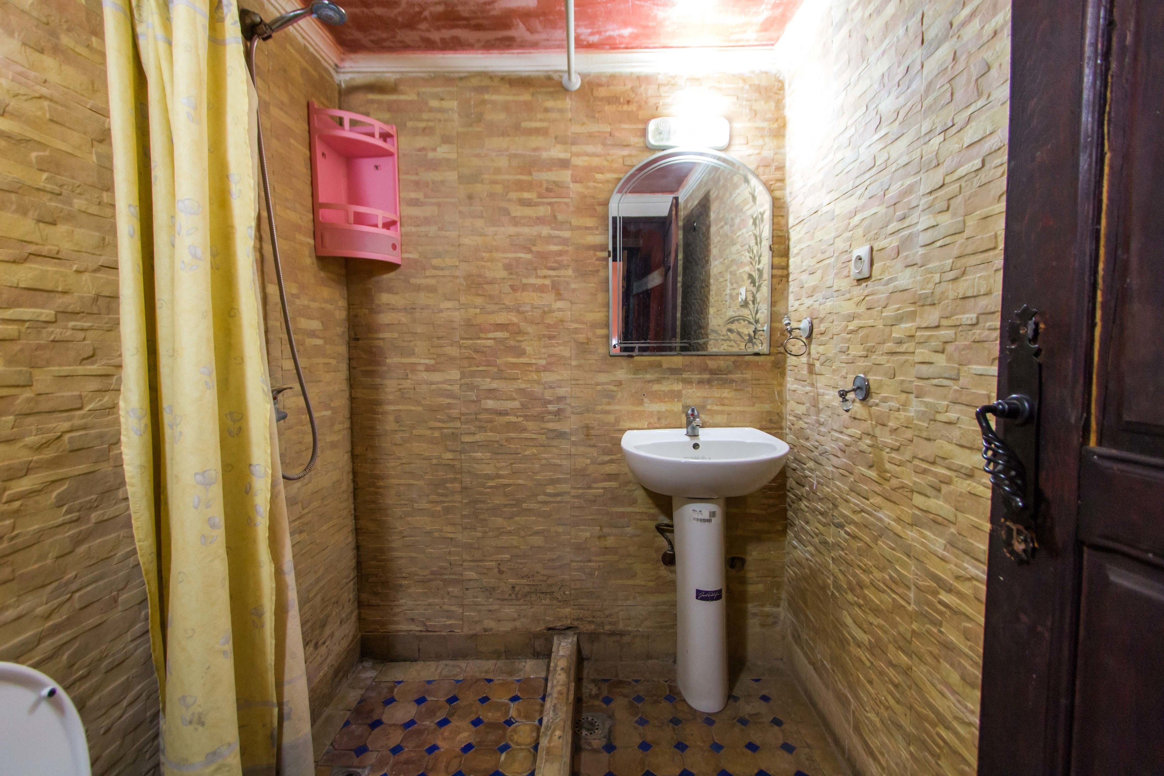 A bathroom with a tiled floor, a sink, a mirror, and a shower curtain.