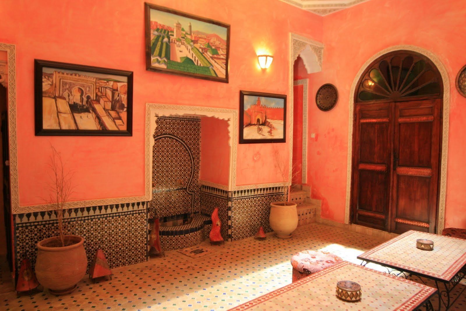 A room with a tiled floor, a large wooden door, and a wall with framed artwork.