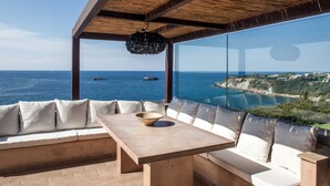 Un espace extérieur ensoleillé, aménagé avec des sièges, offrant une vue sur la mer et une côte lointaine.