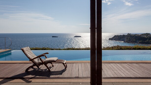Une terrasse en bois avec un fauteuil de relaxation donnant sur une piscine et la mer.