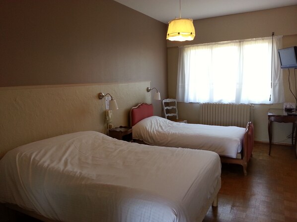 Una habitación de hotel con dos camas, un escritorio con televisor, una lámpara y una ventana con cortinas.