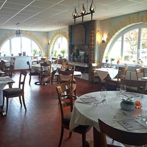 A restaurant with round tables, chairs, and a brick fireplace. - Auberge du Gros (Colligny)