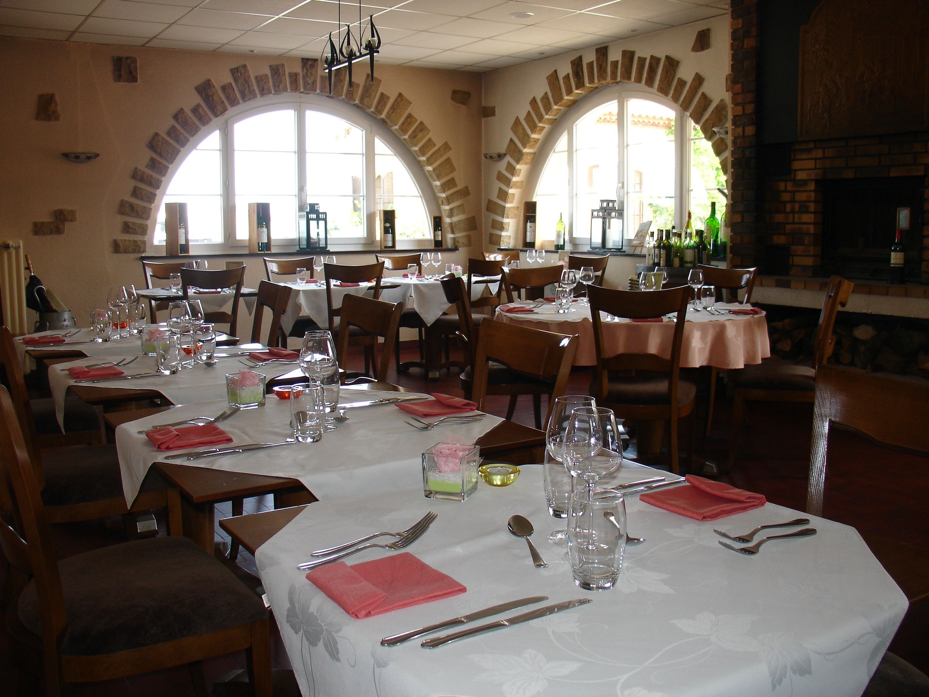 A restaurant with multiple tables set for dining, featuring a brick fireplace and large arched windows.