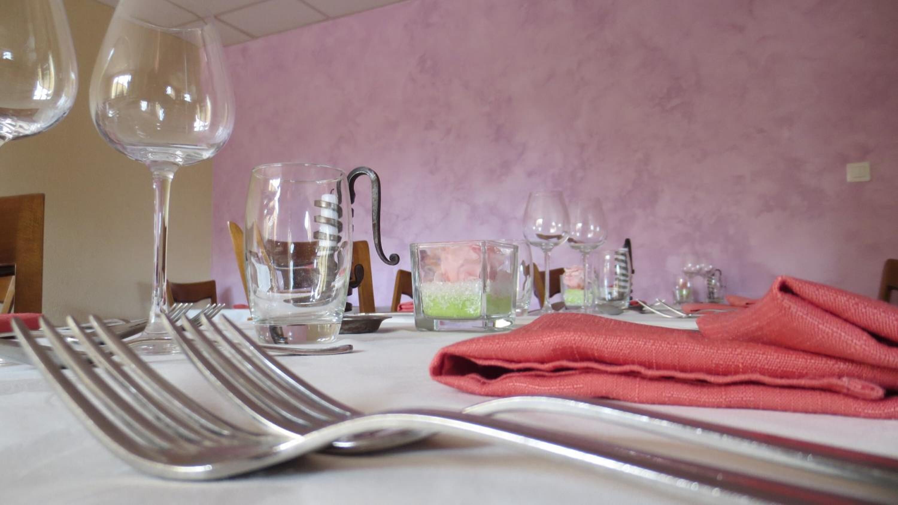 A dining table set with cutlery and glasses, a folded napkin, and a candle in a glass holder.