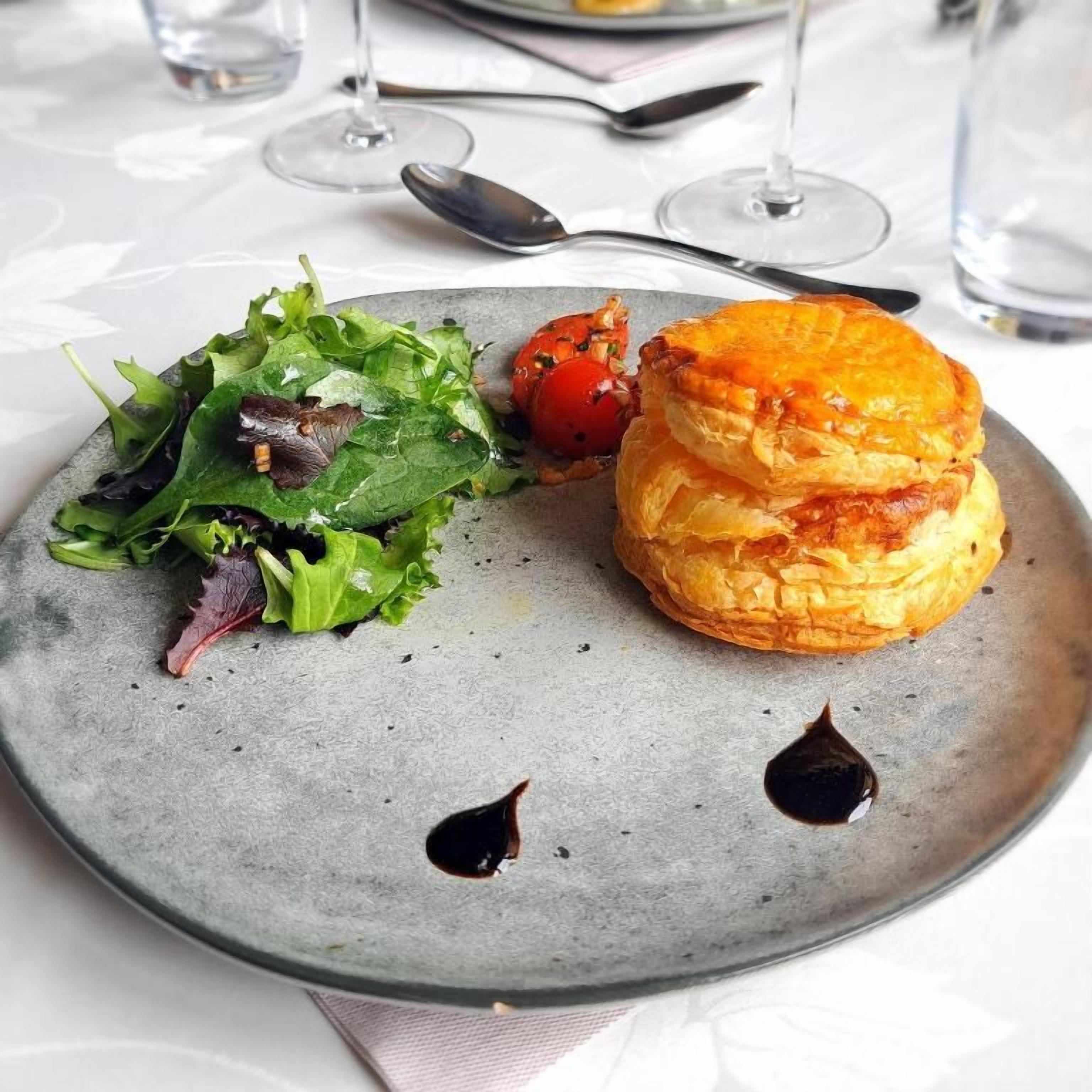 A plate with a pastry and salad, a spoon, and a glass of water on a table.