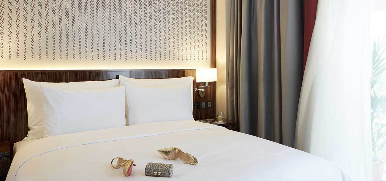 A hotel room with a large bed, a nightstand with a lamp, and a view of the outdoors.