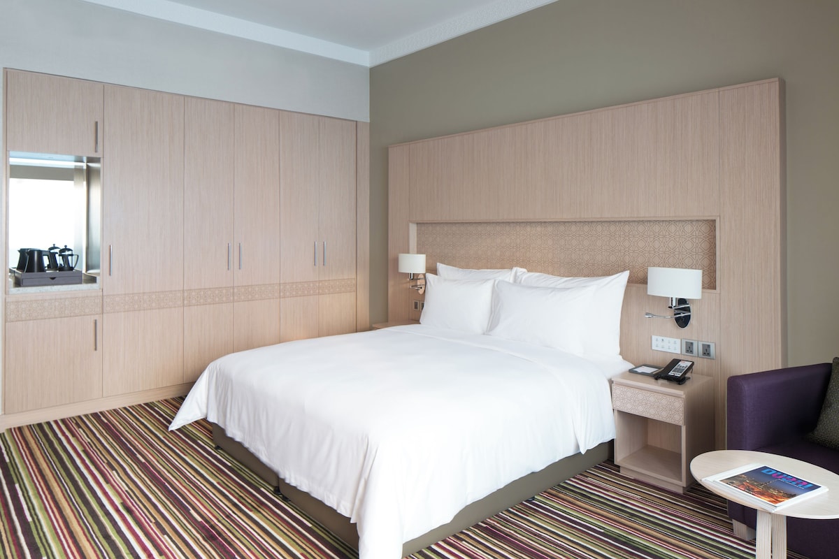 A hotel room with a bed, a nightstand with a lamp, a chair, and a wardrobe.