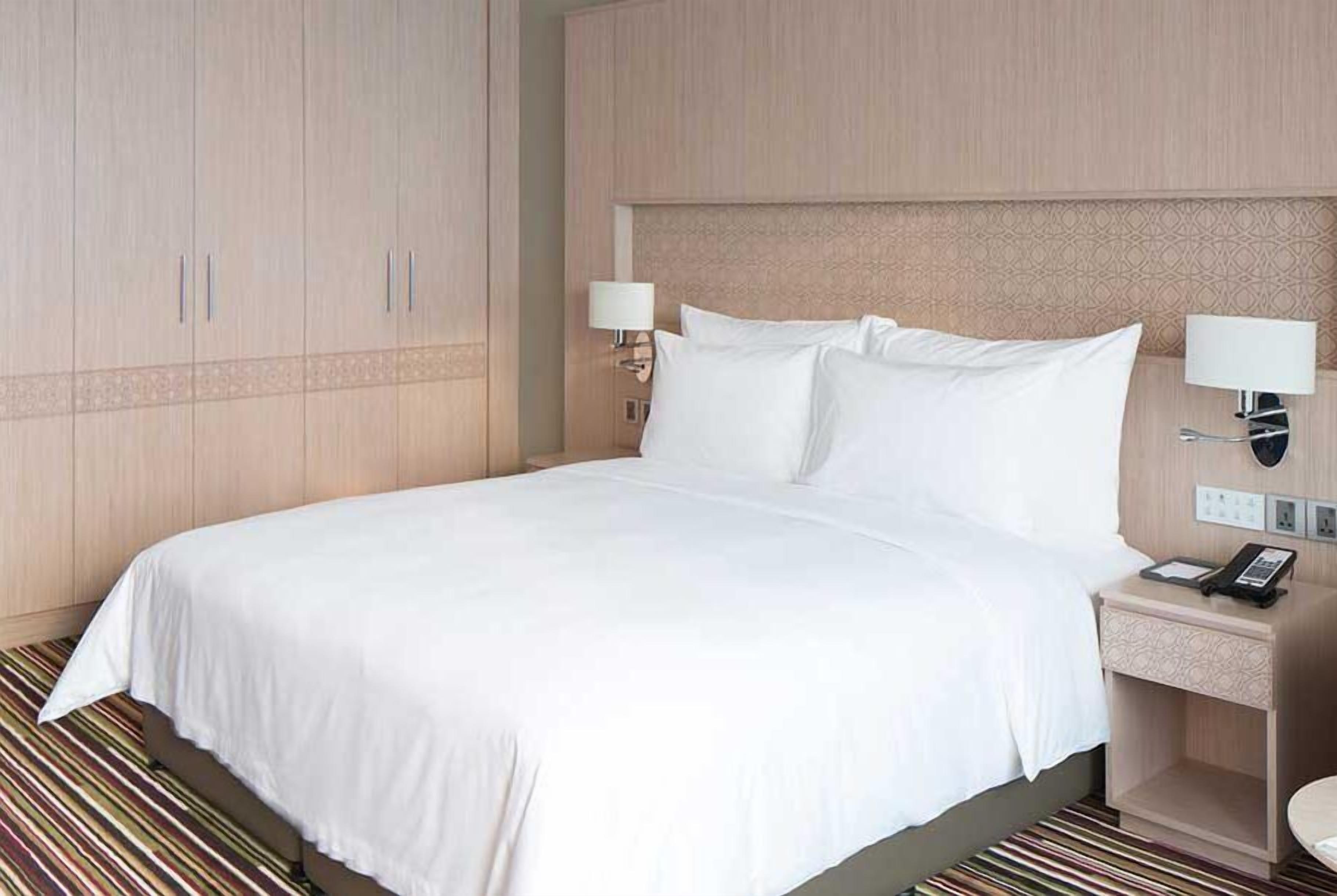 A hotel room with a large bed, two bedside lamps, a nightstand with a phone, and a wardrobe.