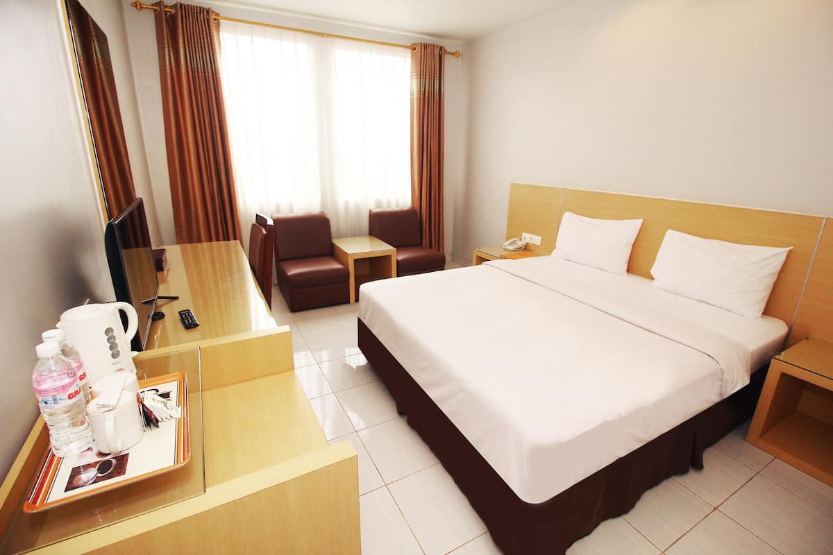 Habitación de hotel con una cama grande, un escritorio con cafetera, una silla, televisor y ventana con cortinas.