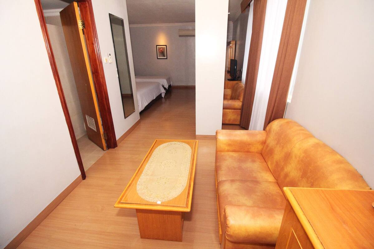 Habitación de hotel con piso de madera, un sofá, una mesita de madera y una cama con ropa blanca.