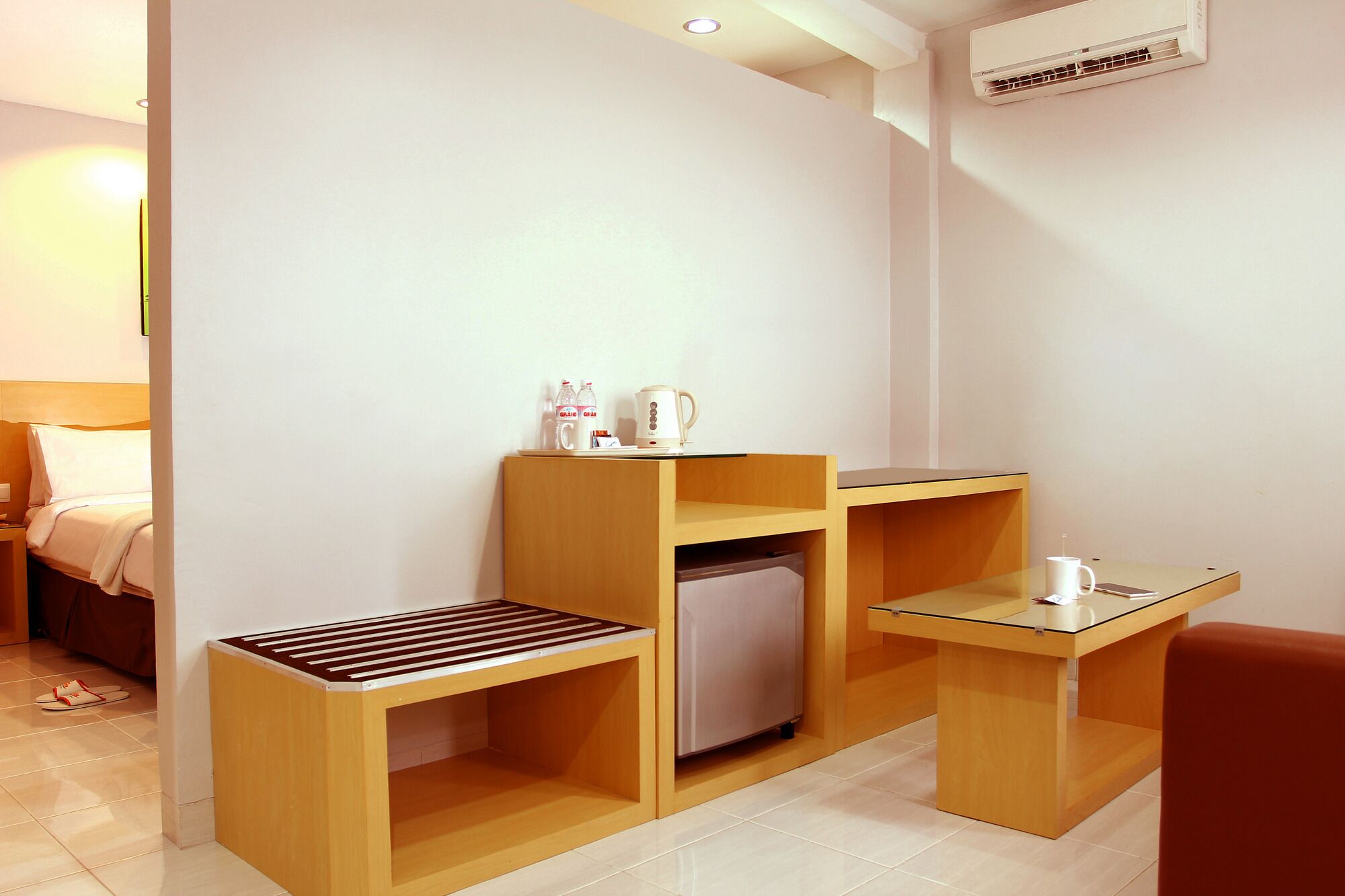 A compact hotel room with a bed, a small kitchenette, a seating area, and a refrigerator.