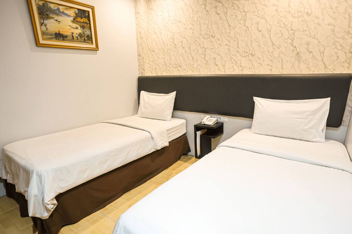 Habitación de hotel con dos camas individuales, una mesita de noche con teléfono y pared con estampado de mármol.