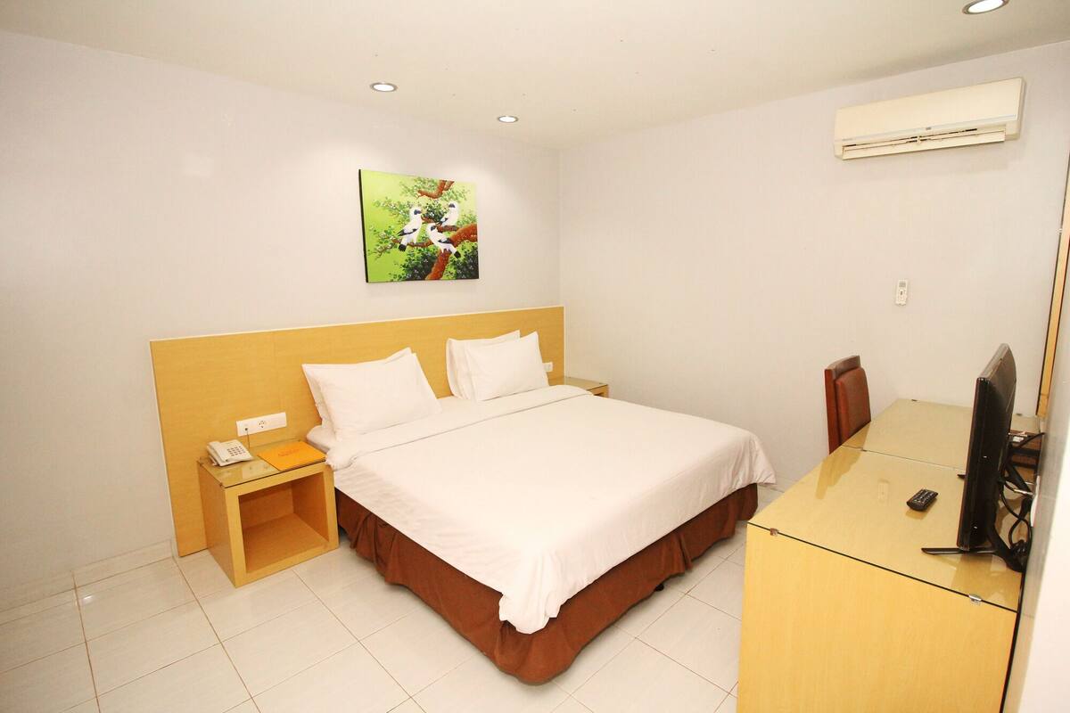 Habitación de hotel con cama, mesita de noche, escritorio con silla, aire acondicionado y un cuadro en la pared.