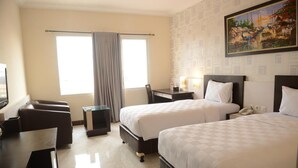 A hotel room with two beds, a desk, a chair, a small table, and a painting on the wall. - Hotel 88 Diponegoro (Jember)