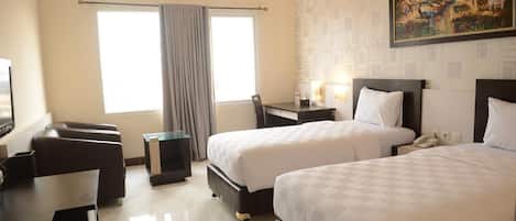 A hotel room with two beds, a desk, a chair, a small table, and a painting on the wall.