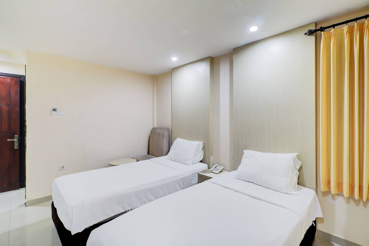 Ein Hotelzimmer mit zwei Einzelbetten, einem Nachttisch mit Telefon, einem Sessel und einem Vorhang.