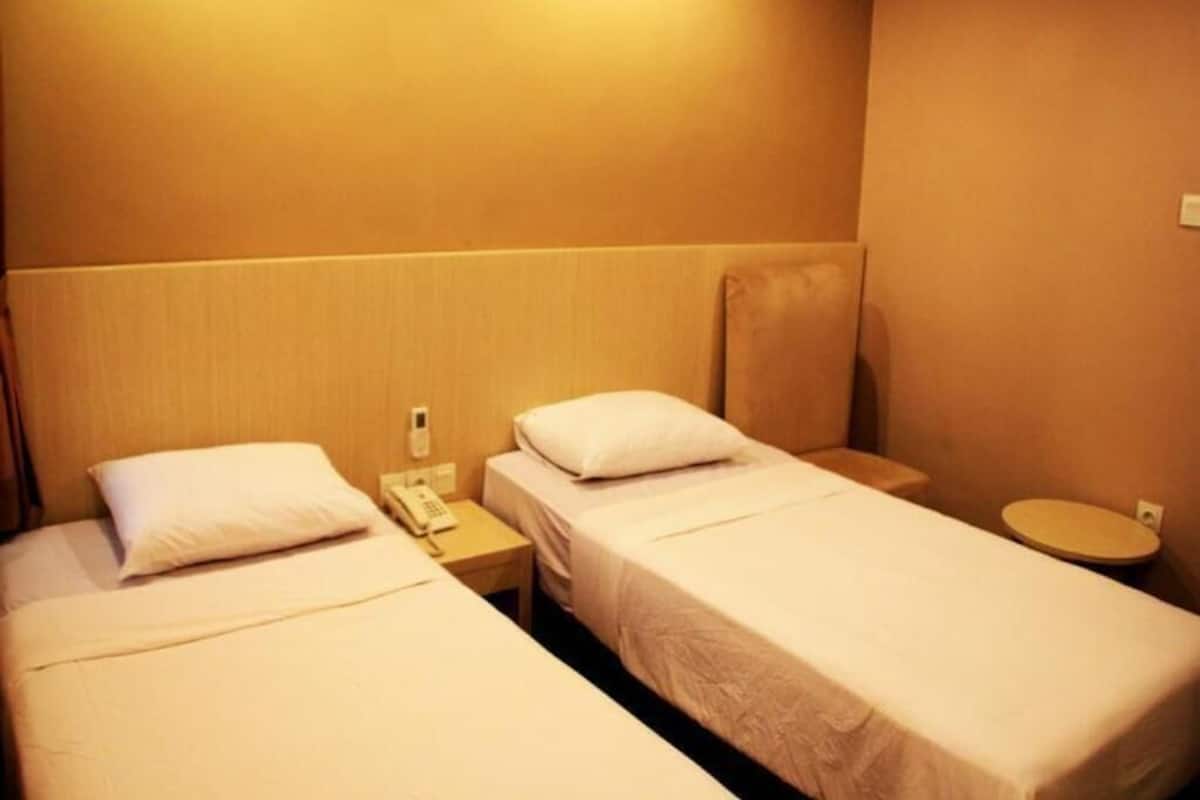 Ein Hotelzimmer mit zwei Einzelbetten, einem Nachttisch mit Telefon und einem kleinen runden Tisch mit Toilette.