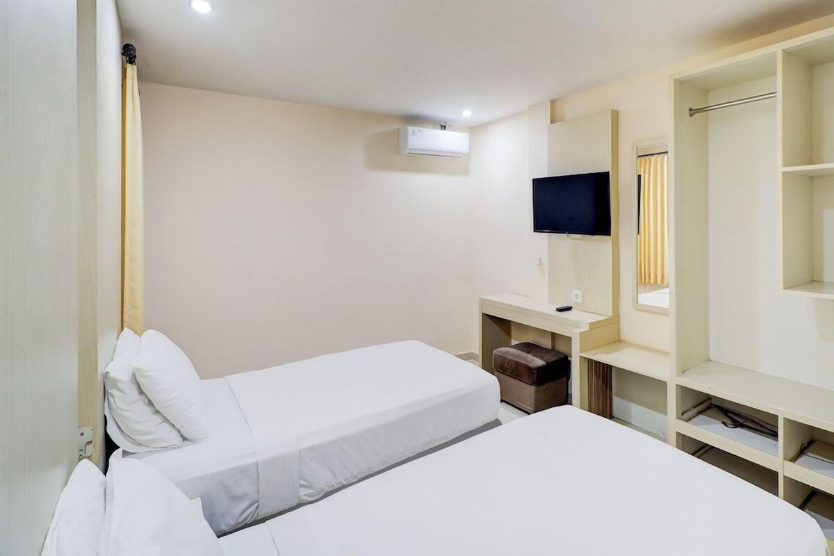A hotel room with two beds, a TV, a wardrobe, and a small desk.