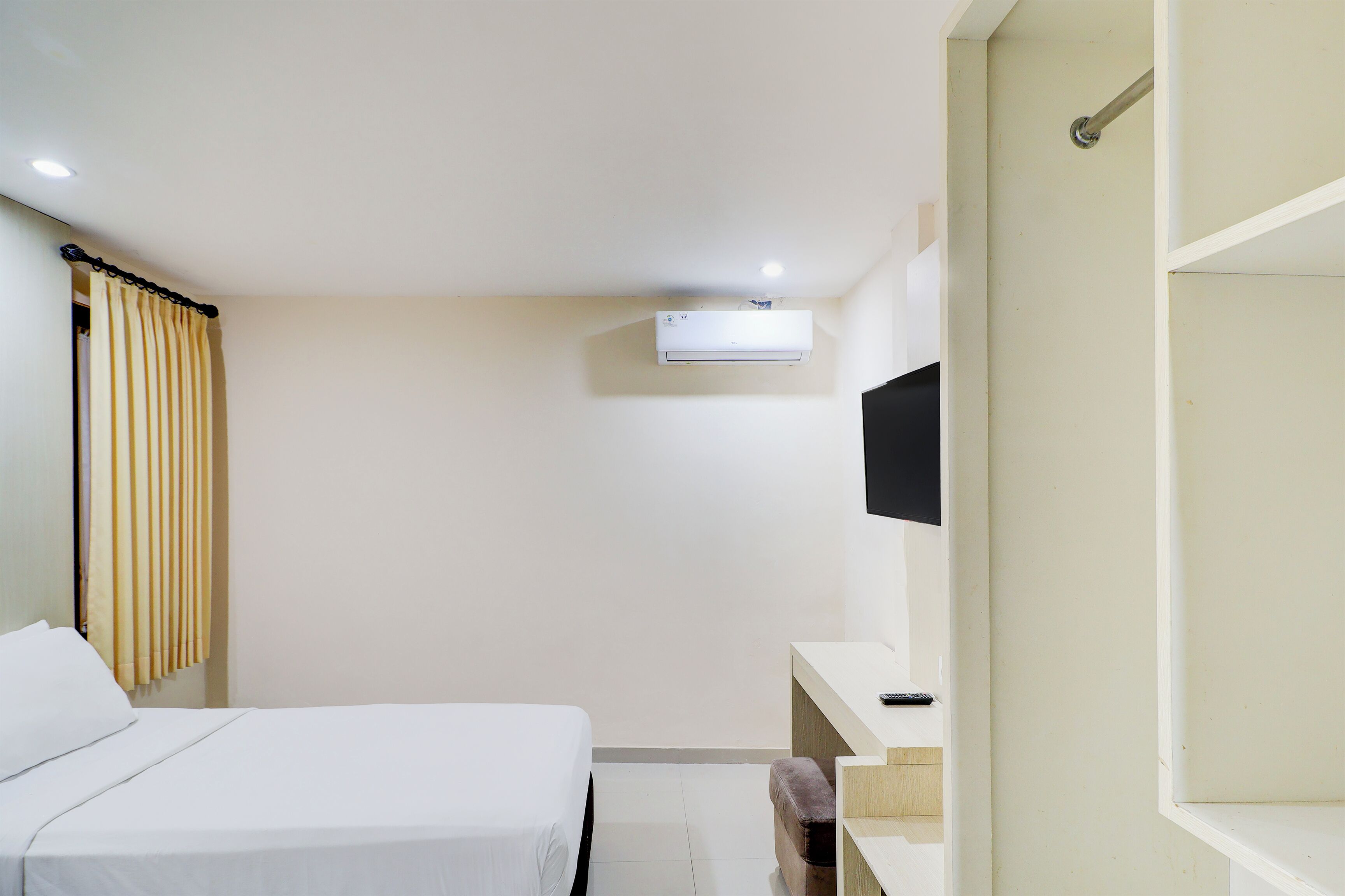 A hotel room with a bed, a desk, a television, and an air conditioning unit.