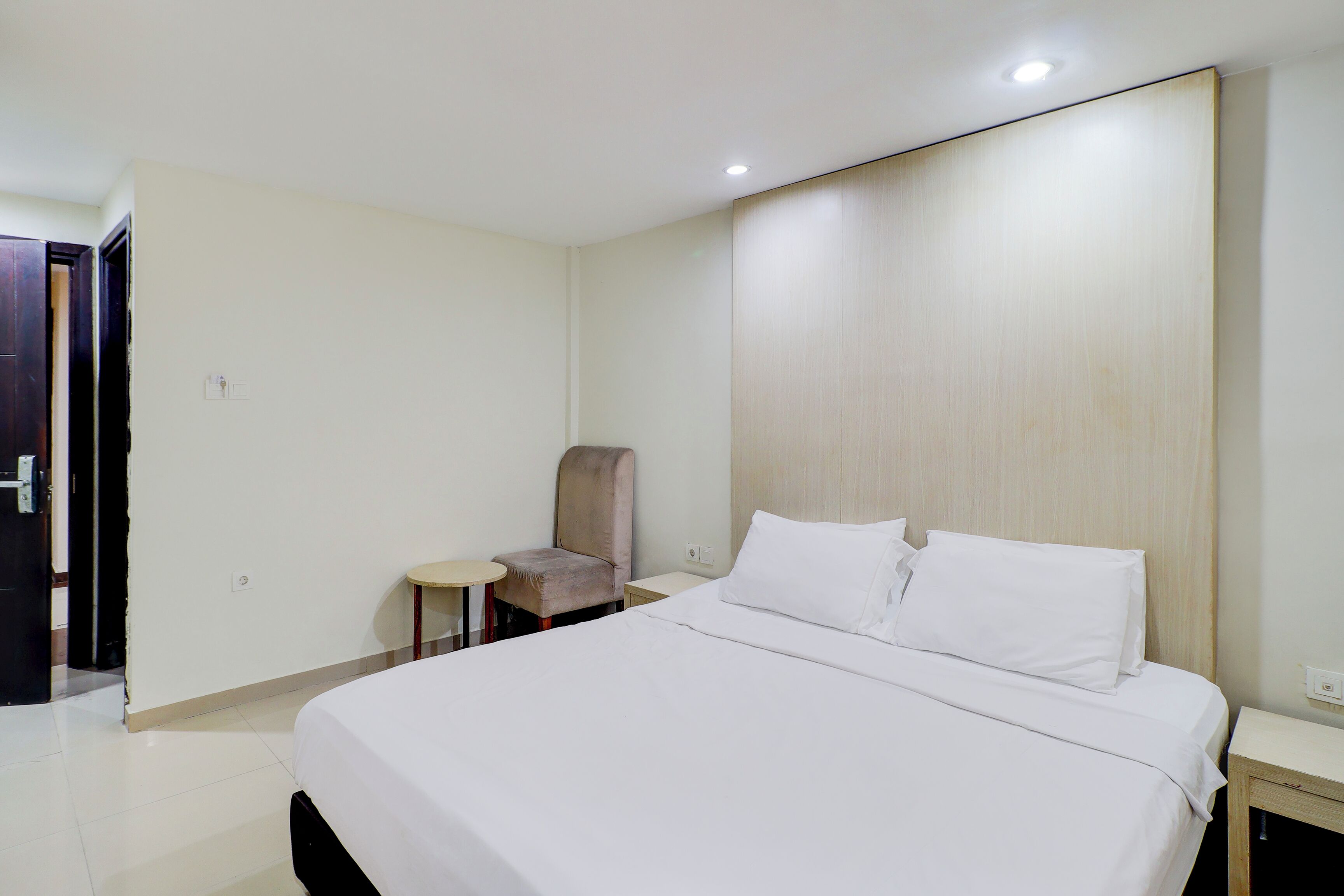 Une chambre d’hôtel avec un lit, une chaise, une petite table et une tête de lit en bois.