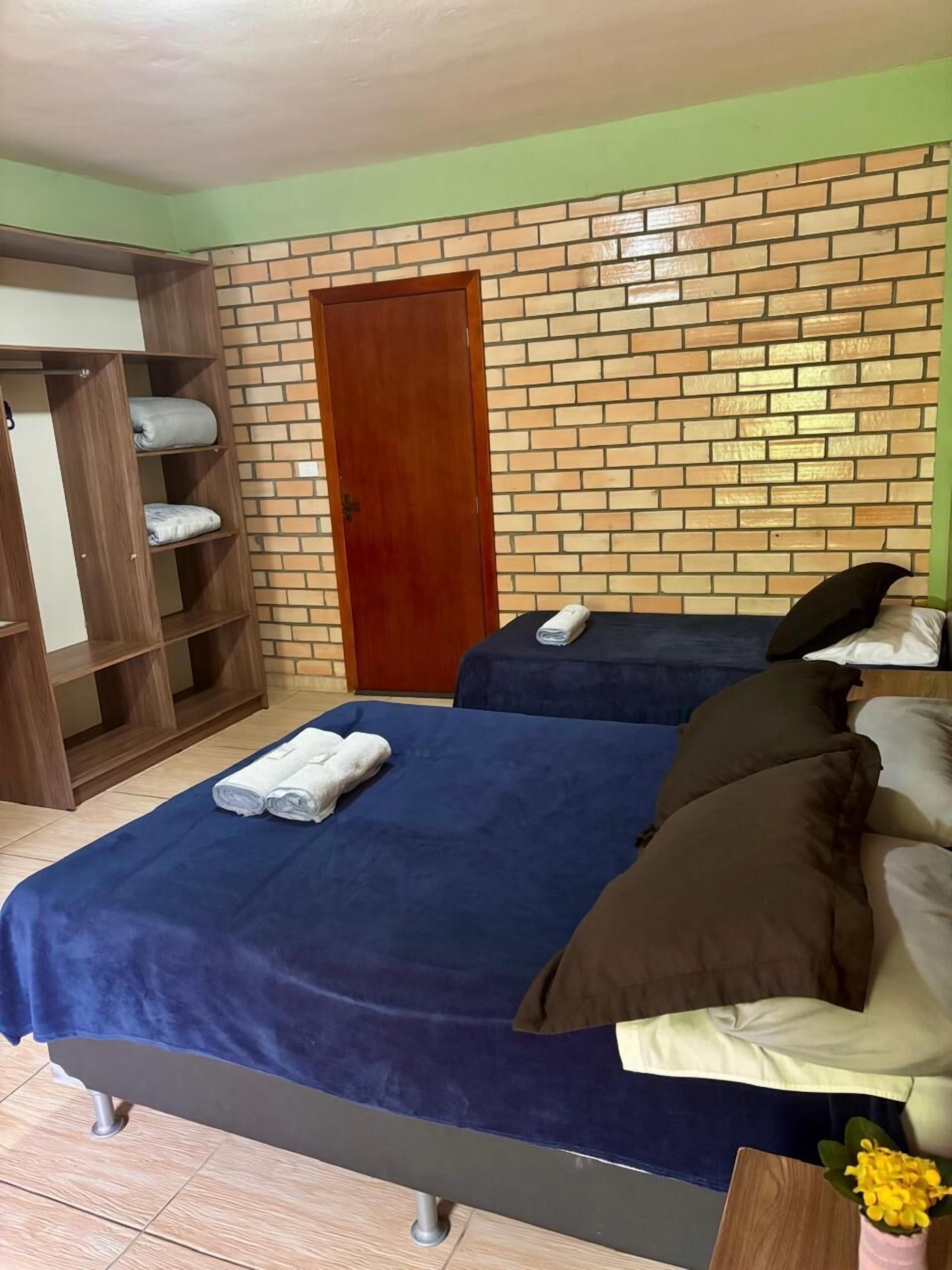 A room with two beds, a wardrobe, and a brick-patterned wall.