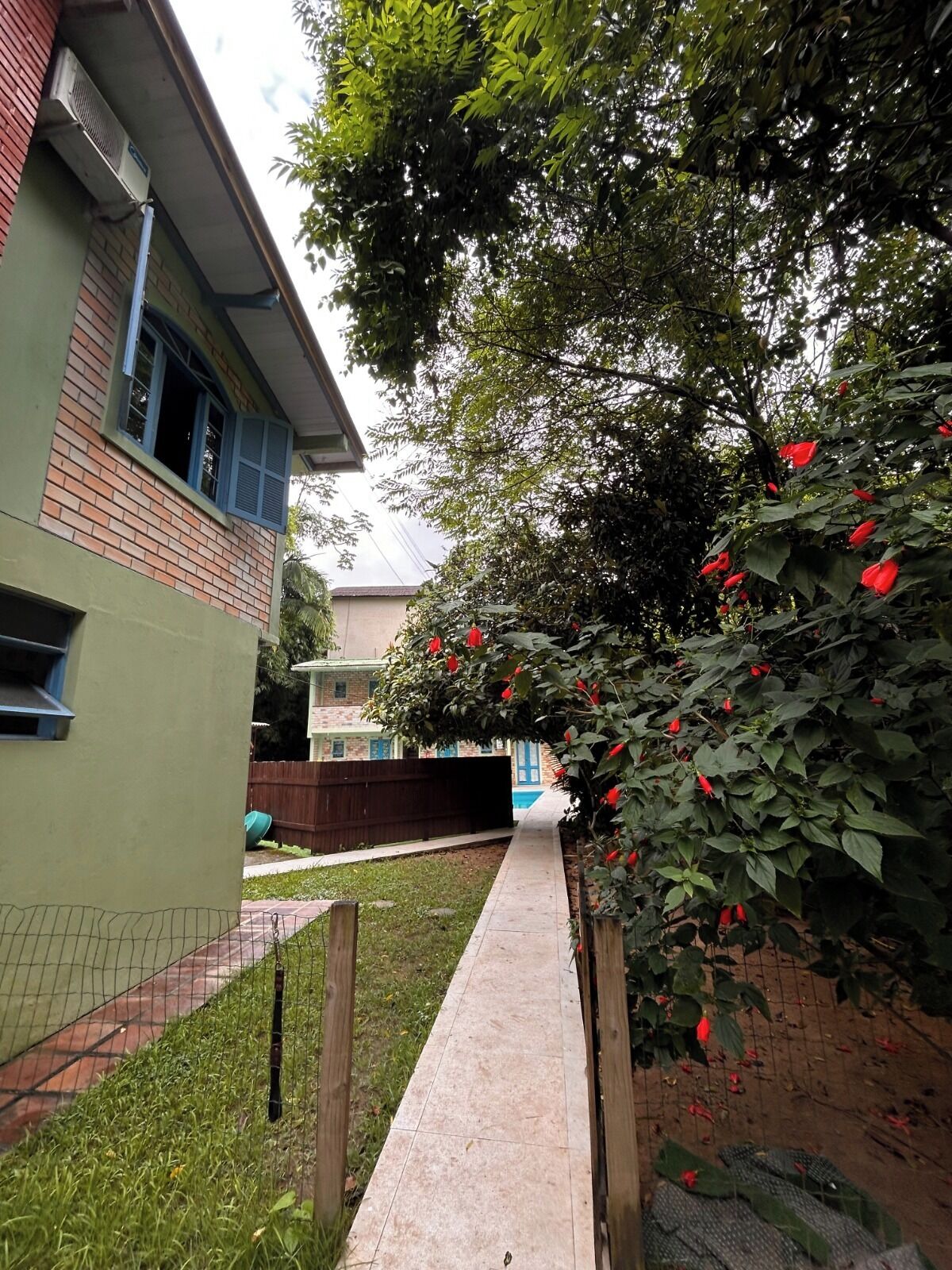 A pathway leading to a building with a brick facade and a window with blue shutters.