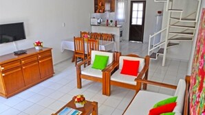 A spacious living area with a sofa, chairs, a coffee table, and a TV. - Residencial Jerusalém I (Porto Seguro)