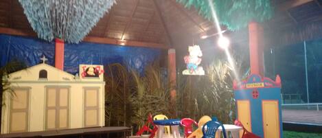 A covered outdoor area with a stage, seating, and colorful play structures.