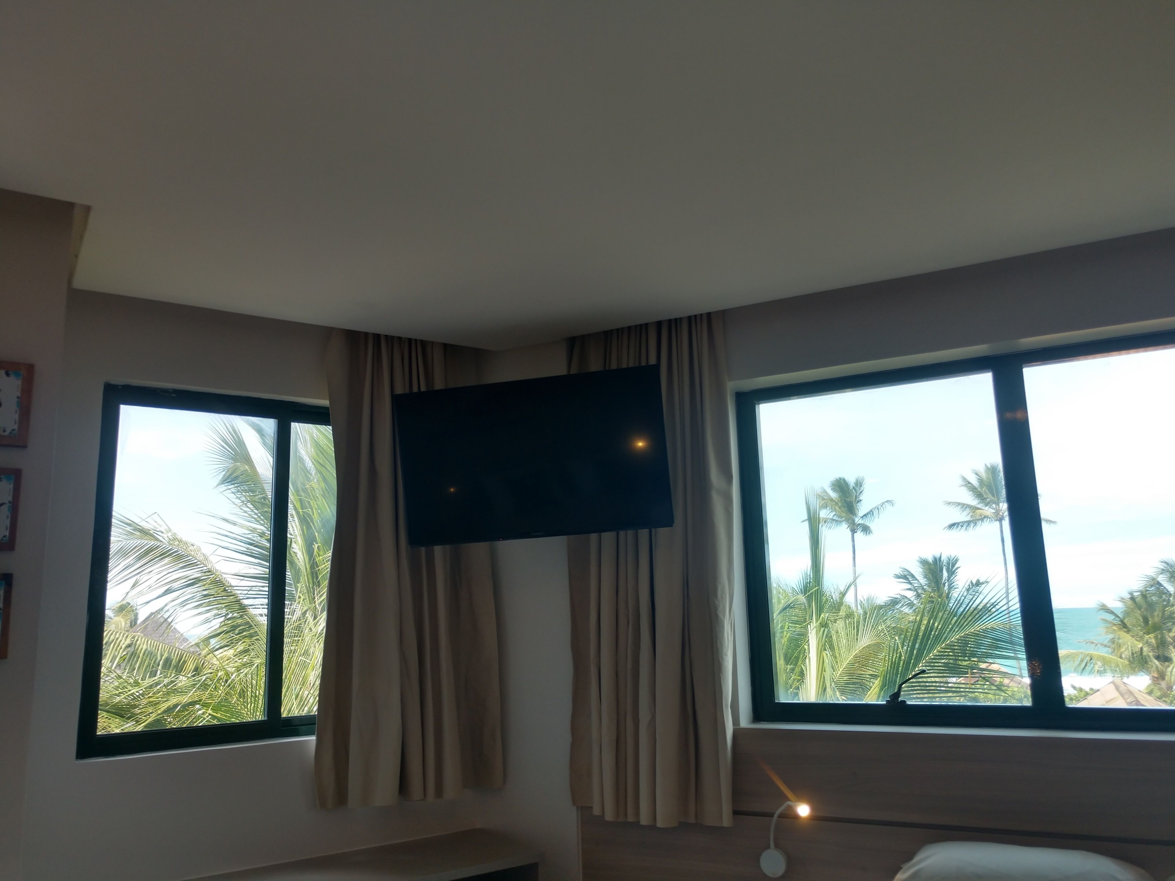 A hotel room with two large windows offering a view of palm trees and the ocean.
