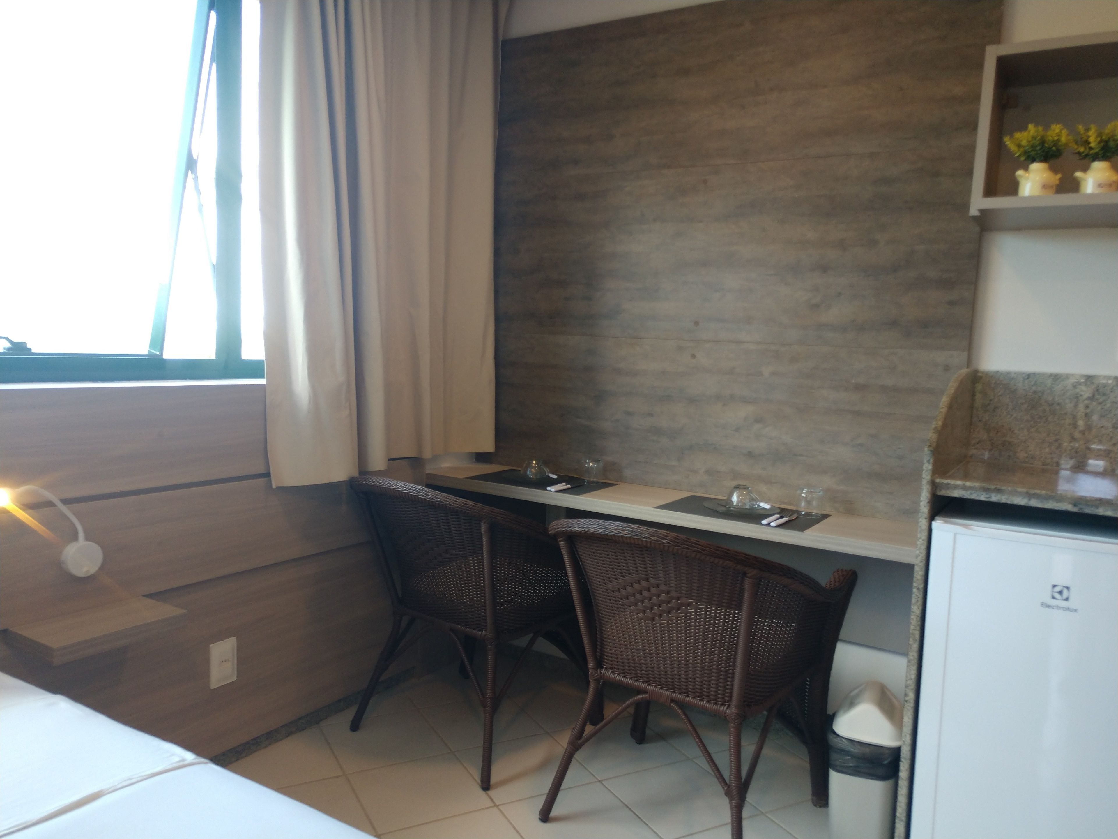 A small kitchenette with a dining area, two wicker chairs, a table, and a refrigerator.