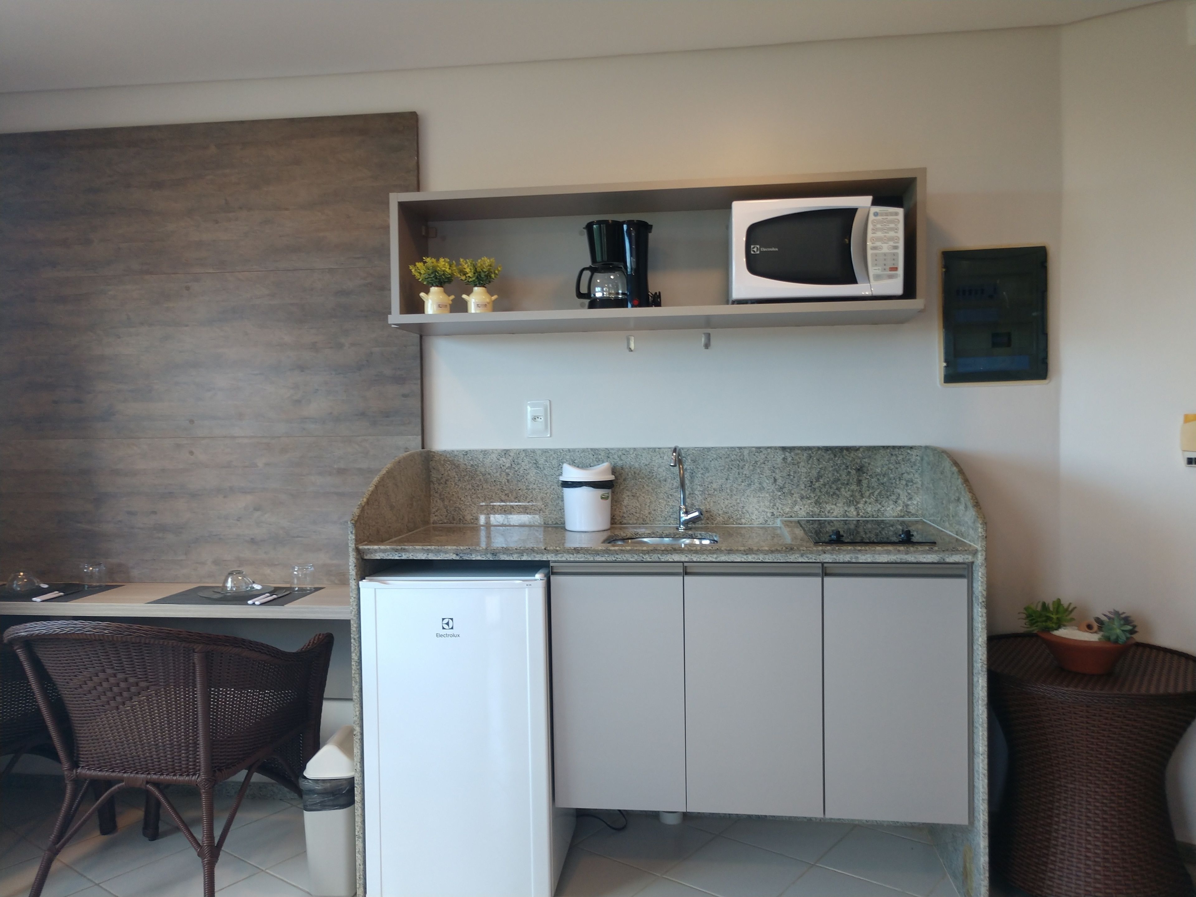 A compact kitchen with a microwave, coffee maker, and small potted plants on the shelf.