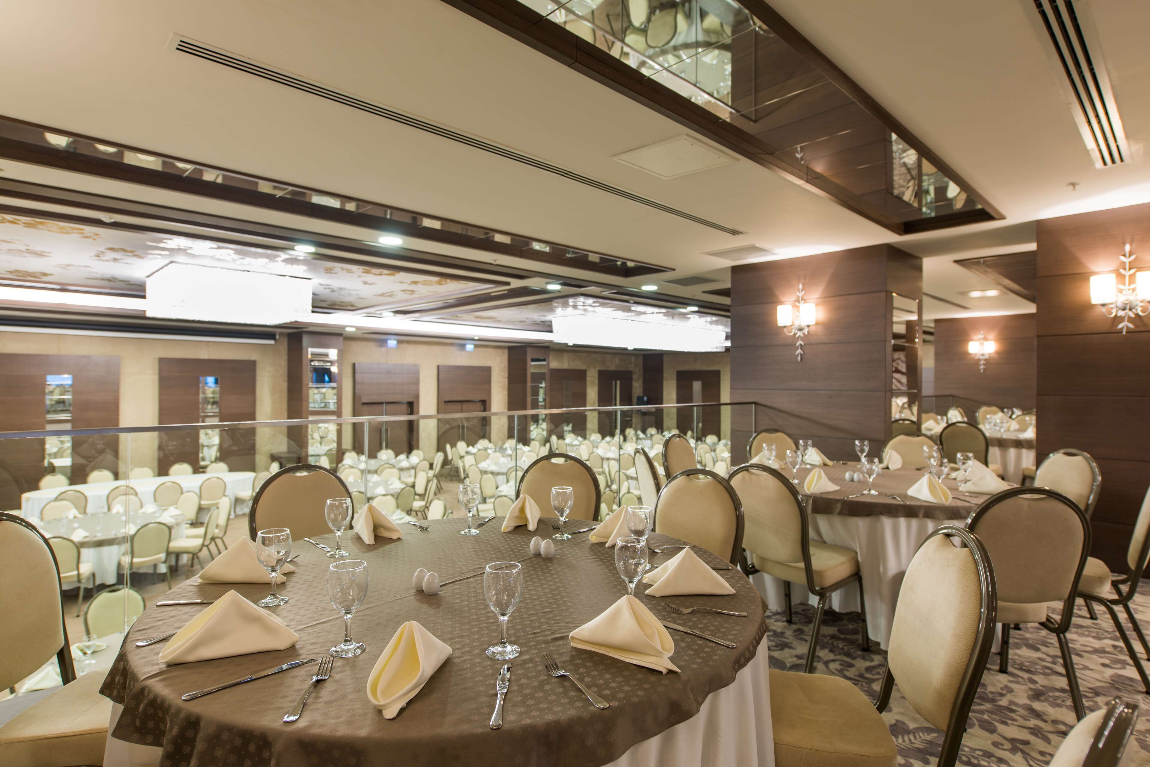Un salón de banquetes con mesas redondas dispuestas para comer, equipado con vasos y servilletas.