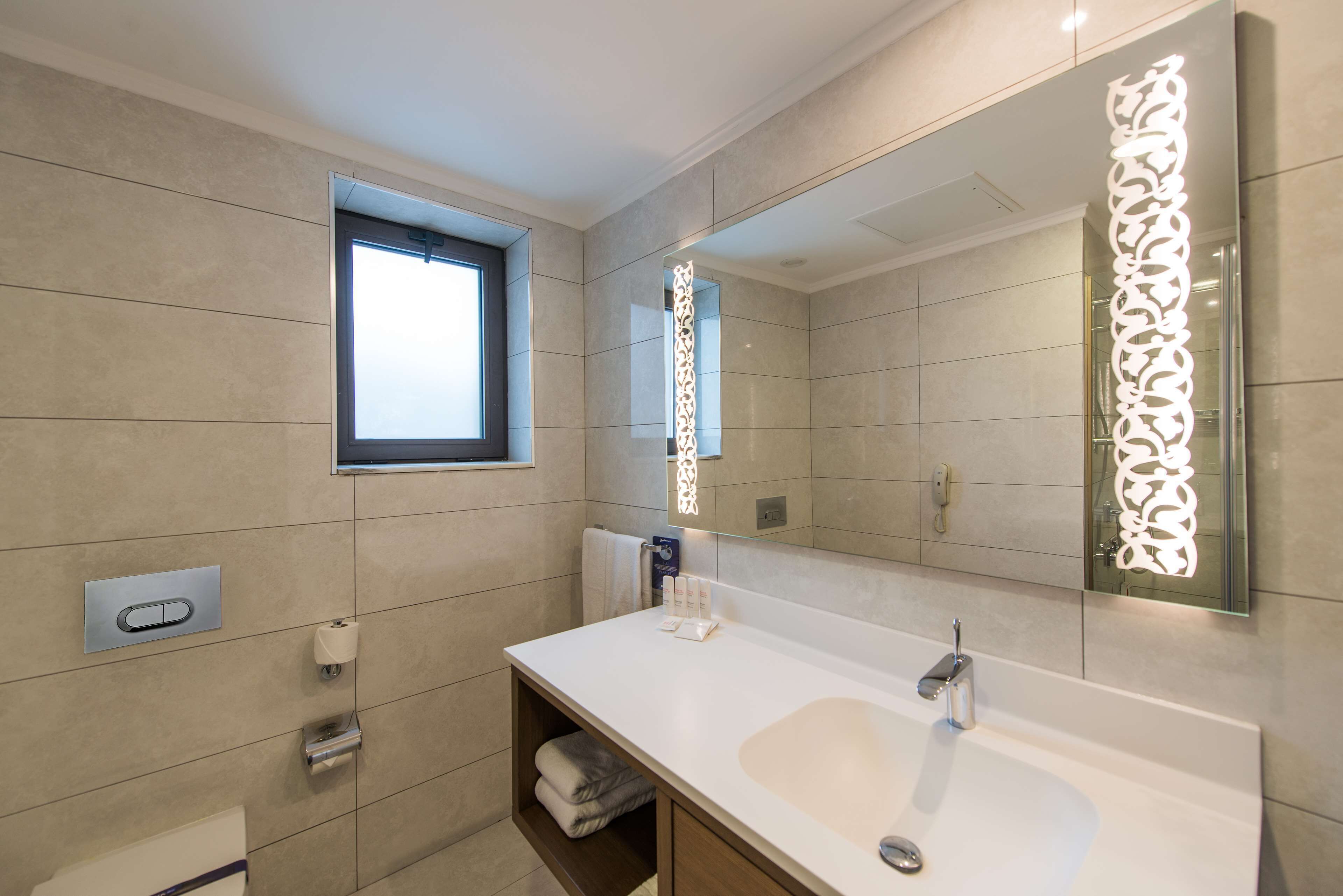 A modern bathroom with a large sink, a window, and a decorative mirror.