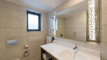 A modern bathroom with a large sink, a window, and a decorative mirror.