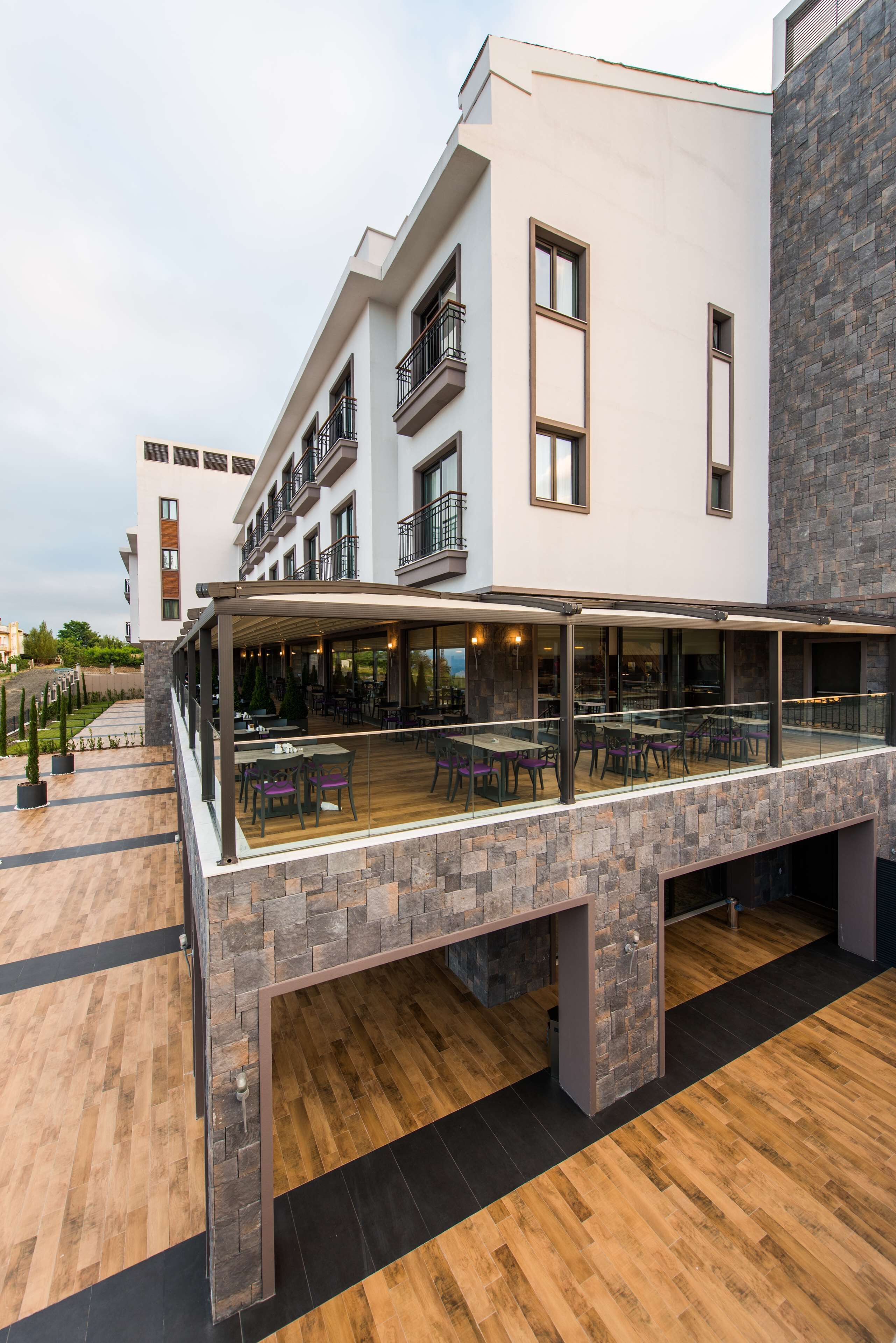 A modern building with a covered outdoor seating area, stone facade, and multiple balconies.