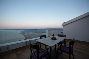 Un balcón con mesa y sillas, con vista a una ciudad costera al atardecer.