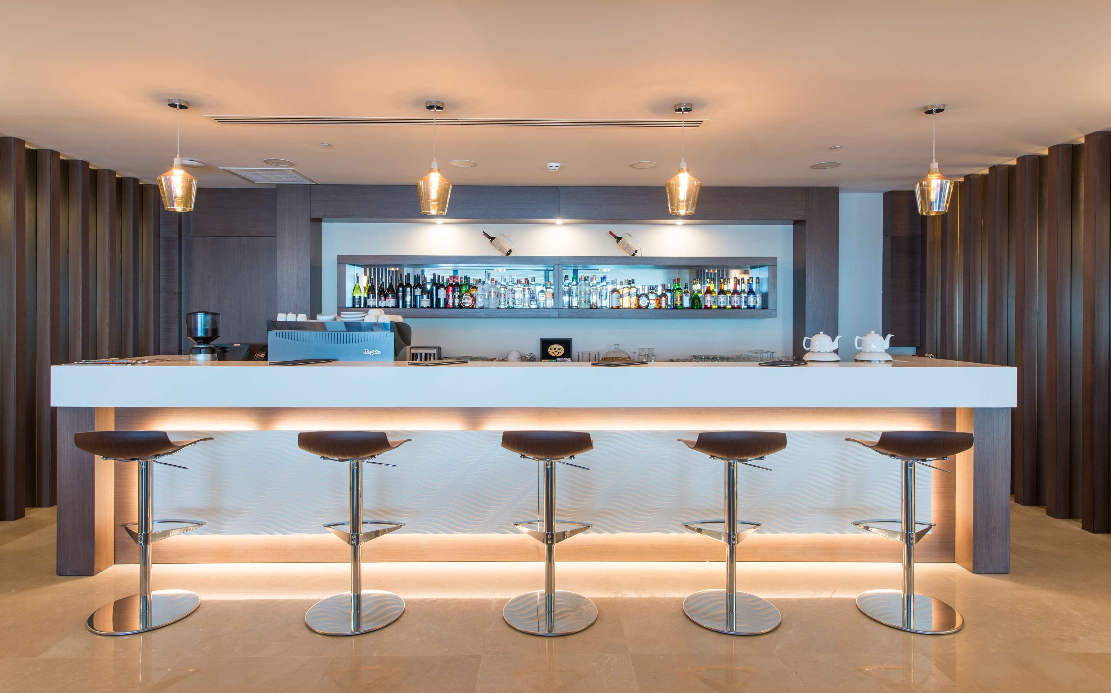 A modern bar area with a long counter, multiple stools, and a well-stocked bar with various bottles.