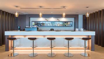 A modern bar area with a long counter, multiple stools, and a well-stocked bar with various bottles.